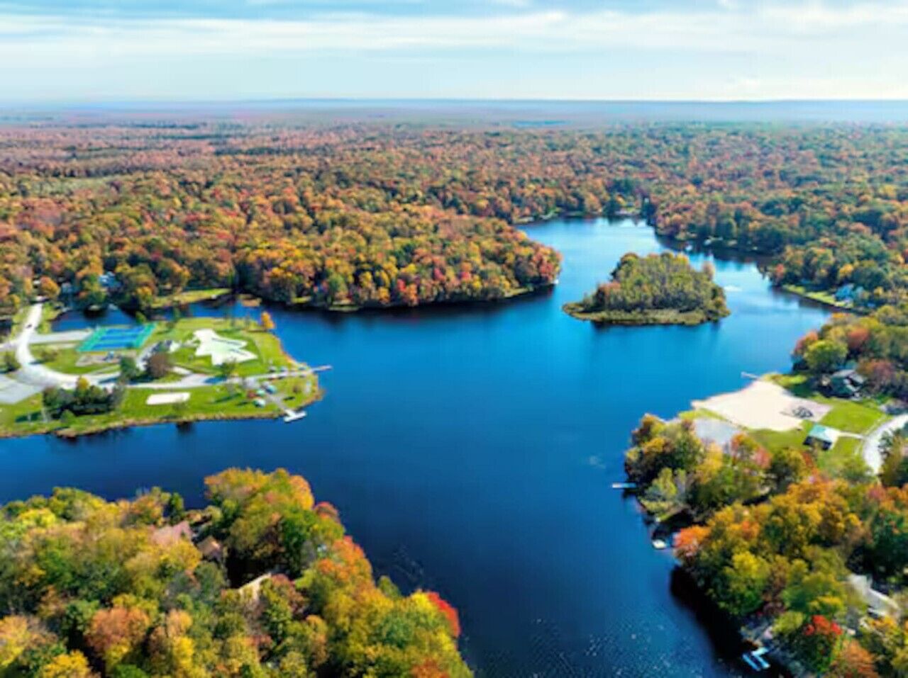 A river surrounded by dense forest, with a small island and a park area with pathways.