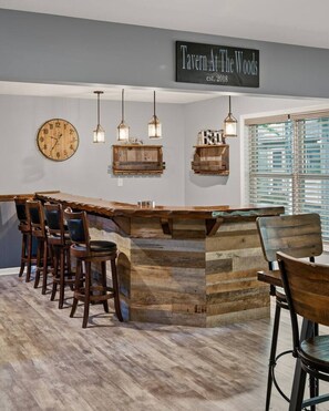 A bar area with a wooden bar counter, hanging pendant lights, and a clock on the wall. - Lake Front Cabin with Hot Tub and Dock (Pocono Lake)