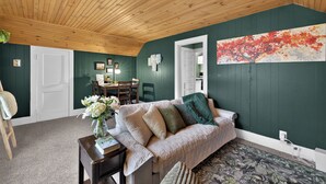 A cozy room with a wooden ceiling, a green wall, a sofa, a table with a vase of flowers, and a painting.