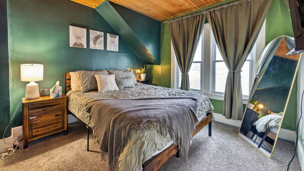 A bedroom with a bed, nightstand, lamp, and a mirror reflecting the room.