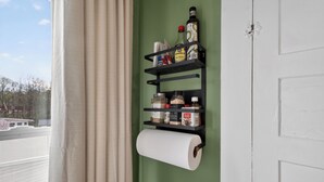 A bathroom with a toilet paper holder, shelves with various toiletries, and a view of a building outside.