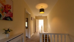 A hallway with a white railing, a ceiling light, and a door leading to another room. - Red House - Private Bathroom (Hinton)