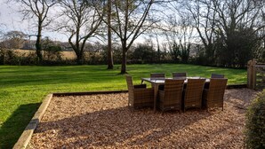 A patio with a table and chairs, surrounded by a grassy area and trees. - Red House - Private Bathroom (Hinton)