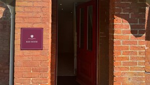 A brick building entrance with a red door, a welcome mat, and a sign reading 'HINTON ADMIRAL RED HOUSE.' - Red House - Private Bathroom (Hinton)