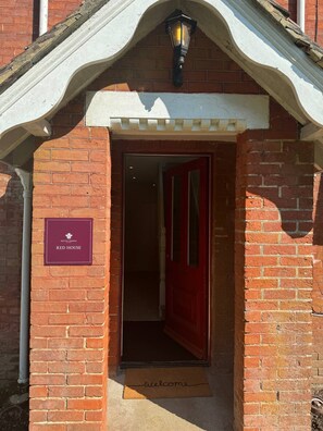 Entree van een bakstenen gebouw met een rode deur, een welkomstmat en een bord waarop 'HINTON ADMIRAL RED HOUSE' staat.