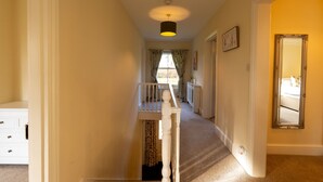 A hallway with a staircase leading to a bedroom. There is a white dresser, a mirror, and a radiator on the wall. - Red House - Private Bathroom (Hinton)