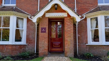 A red brick building with a central entrance, two side windows, and a small porch area.