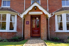 A red brick building with a central entrance, two side windows, and a small porch area.