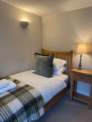 Un lit bien fait, avec une couverture à carreaux, une tête de lit en bois, une lampe de chevet et un luminaire fixé au mur.