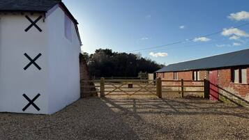 A gravel driveway leading to a gated area with a white building marked with black crosses, a red barn, and a clear sky.