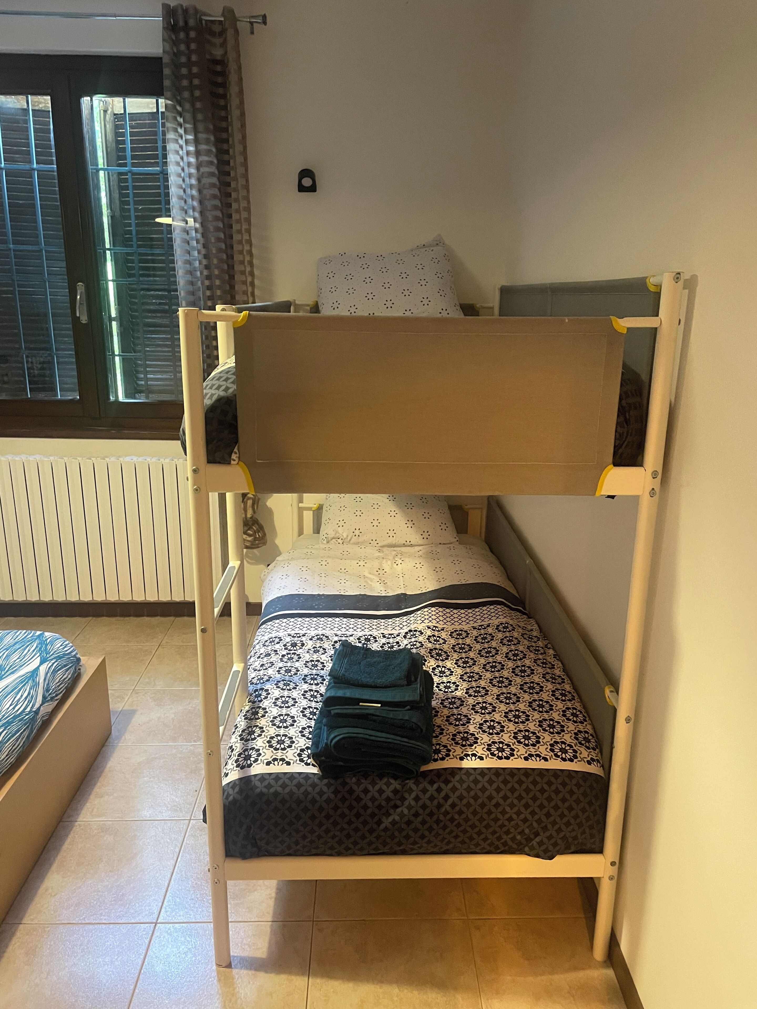 A bunk bed with a mattress and pillows, a small table, and a window with curtains.