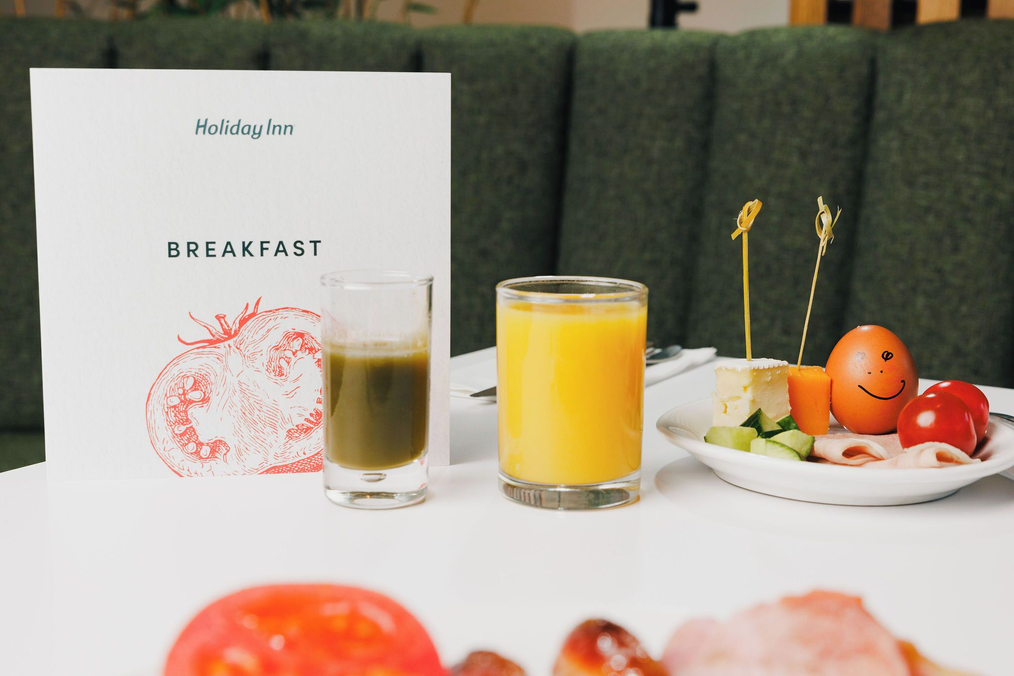 A breakfast setting with a menu card labeled 'Holiday Inn' and a plate of food including eggs, tomatoes, and a glass of orange juice.