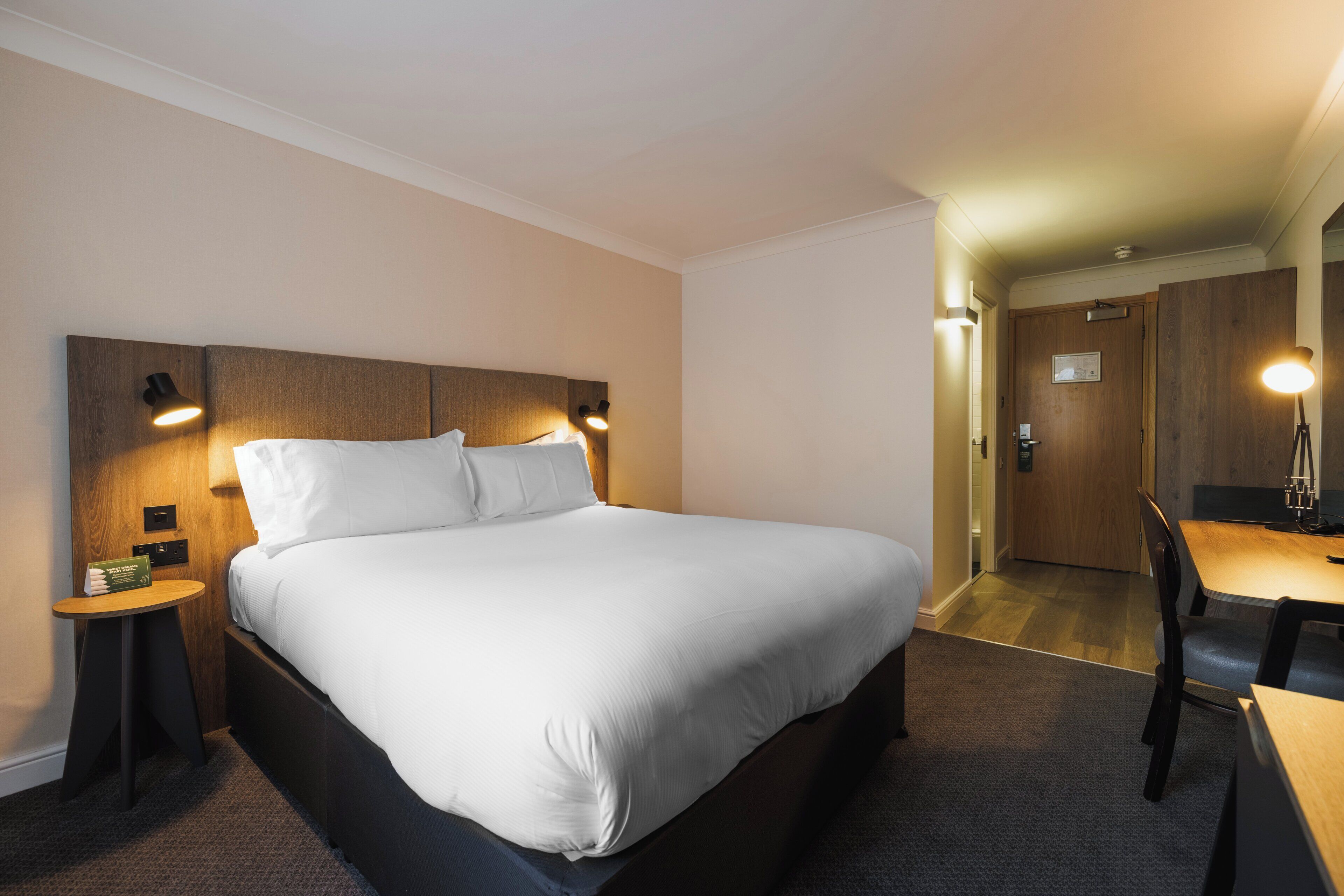 Une chambre d’hôtel avec un grand lit, des tables de chevet, un bureau et une chaise.