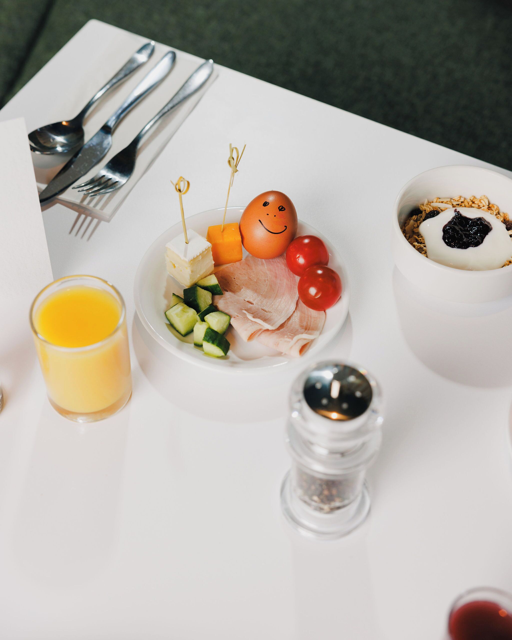 A white table with a plate of food, a glass of orange juice, a salt shaker, and a bowl of yogurt with berries.