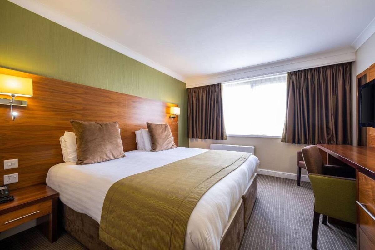 Ein Hotelzimmer mit einem großen Bett, Nachttischlampen, einem Schreibtisch und einem Fernseher.