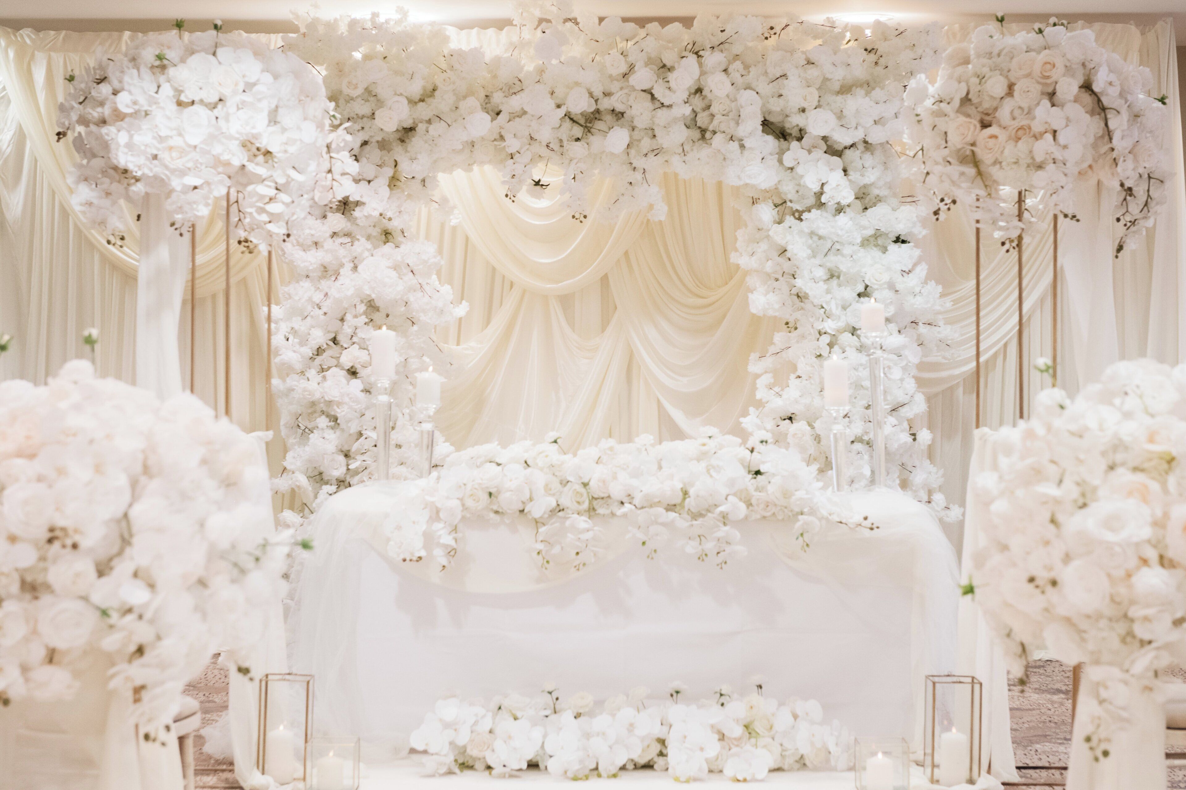 An indoor venue with a stage decorated with white flowers and draped fabric.