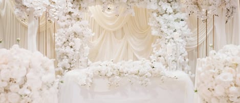 An indoor venue with a stage decorated with white flowers and draped fabric.