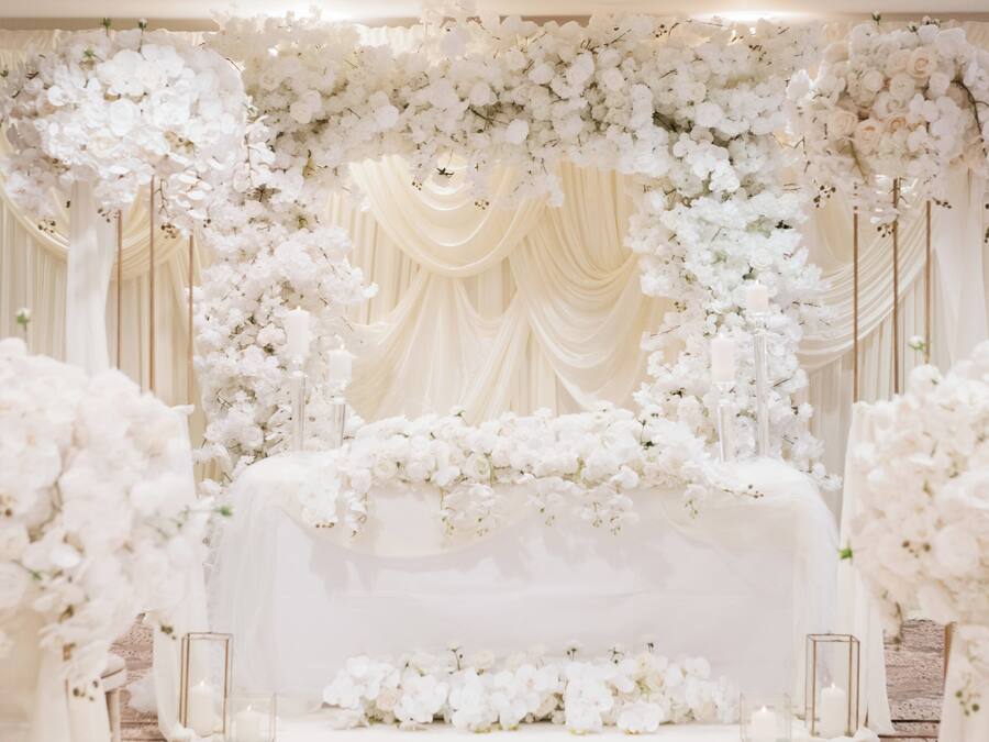 Um espaço interno com palco decorado com flores brancas e tecido drapeado.