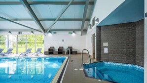 An indoor swimming pool with clear glass walls, a tiled floor, and a ceiling with metal beams. - Holiday Inn Newcastle South by IHG (East Boldon)