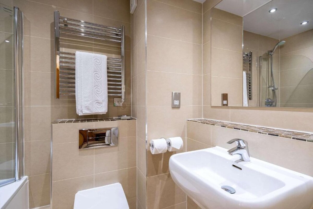 Une salle de bain moderne avec une douche à parois de verre, un lavabo blanc et un porte-serviettes avec une serviette blanche.