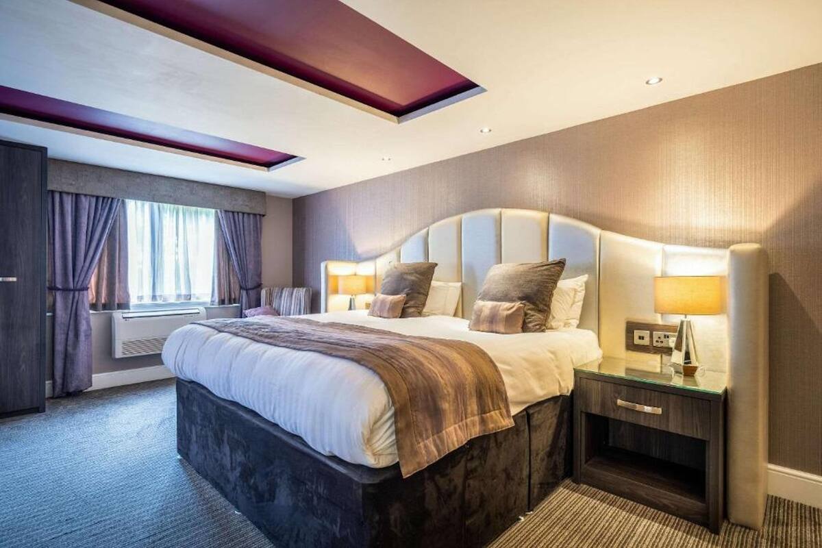 Ein modernes Hotelzimmer mit einem großen Bett, Nachttischen und einem Fenster mit Vorhängen.