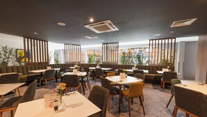 A modern dining area with booths and tables, large windows, and a patterned carpet. - Holiday Inn Newcastle South by IHG (East Boldon)