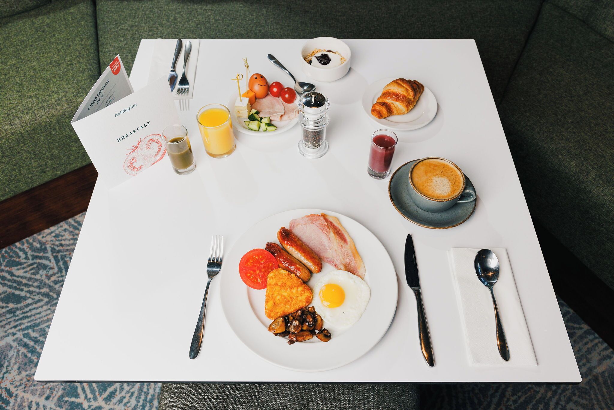 A breakfast setup with a plate of eggs, sausages, and mushrooms, a croissant, and a glass of orange juice.