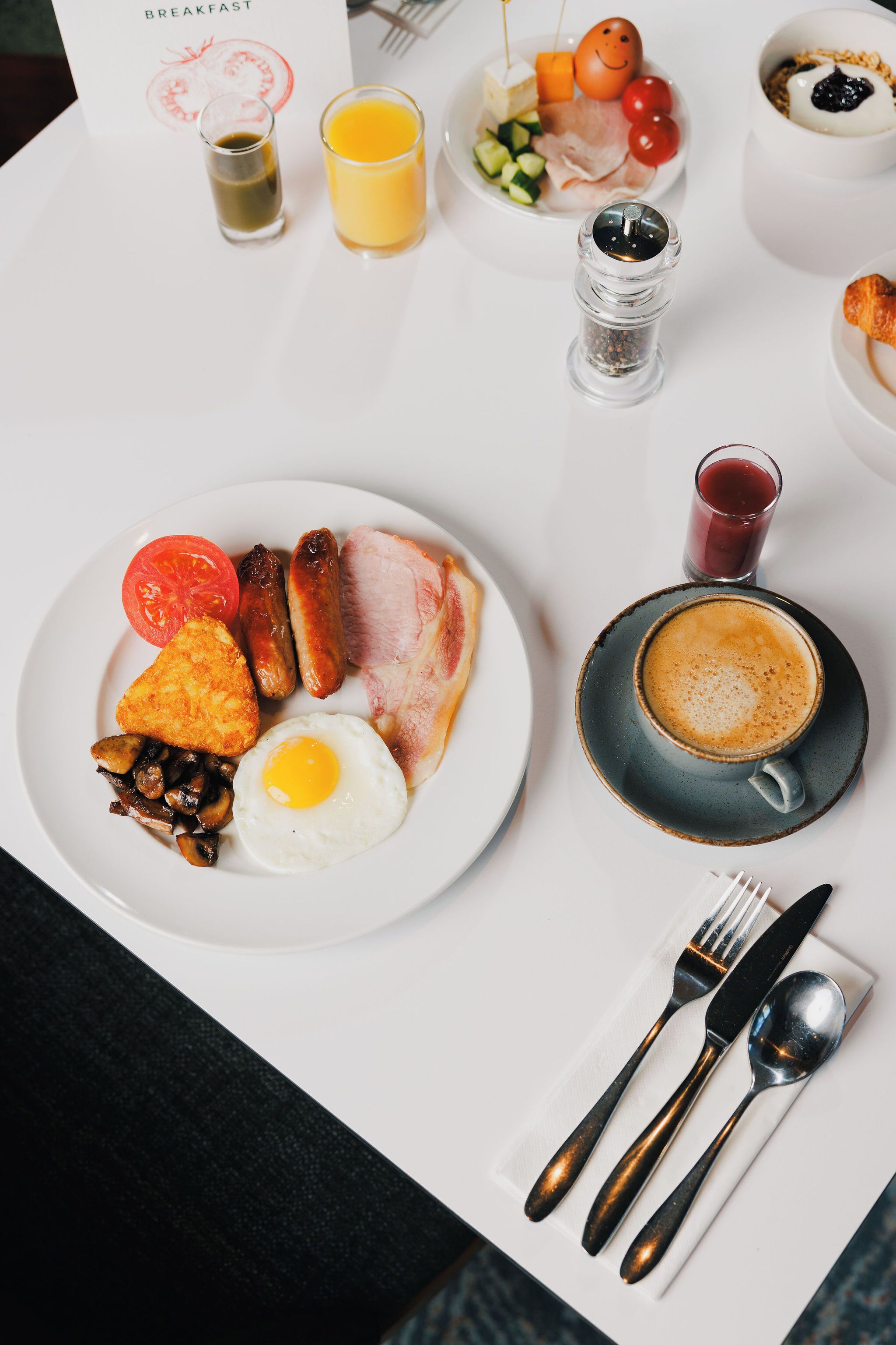 A breakfast setting with a plate of eggs, sausages, and mushrooms, a cup of coffee, and a glass of orange juice.