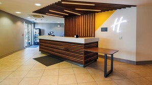 A reception desk with a modern design, a bench, and a clock on the wall. - Holiday Inn Newcastle South by IHG (East Boldon)
