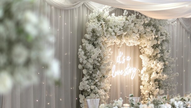 A wedding arch decorated with white flowers and a neon sign that reads "It's a lovely wedding." - Holiday Inn Newcastle South by IHG (East Boldon)