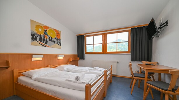 A hotel room with two single beds, a wooden desk with a chair, a window with curtains, and a painting on the wall. - Schmitten 27 - Room 4 200m From ski Lift (Zell am See)