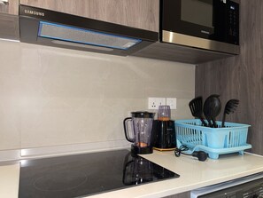 Cozinha com micro-ondas embutido, liquidificador Kenwood e suporte azul para utensílios na bancada.