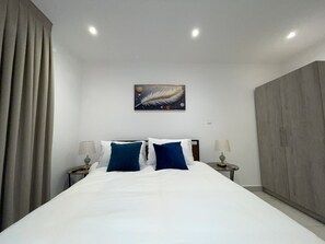 Quarto de hotel com uma cama grande, duas mesas de cabeceira, um quadro na parede e um guarda-roupa.
