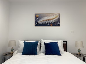 A hotel room with a bed, two nightstands, a lamp on each, and a wall art piece above the bed. - Cozy One-Bedroom Apartment at The Bantree Airport Residential Accra (Accra)
