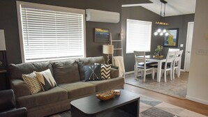 Ein modernes Wohnzimmer mit einem grauen Sofa, einem schwarzen Couchtisch und einem Essbereich mit weißen Stühlen und einem Tisch.