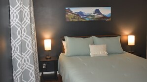 Ein Schlafzimmer mit einem Bett, zwei Nachttischlampen, einem Nachttisch, einem Wandbild und einem Vorhang mit Muster.