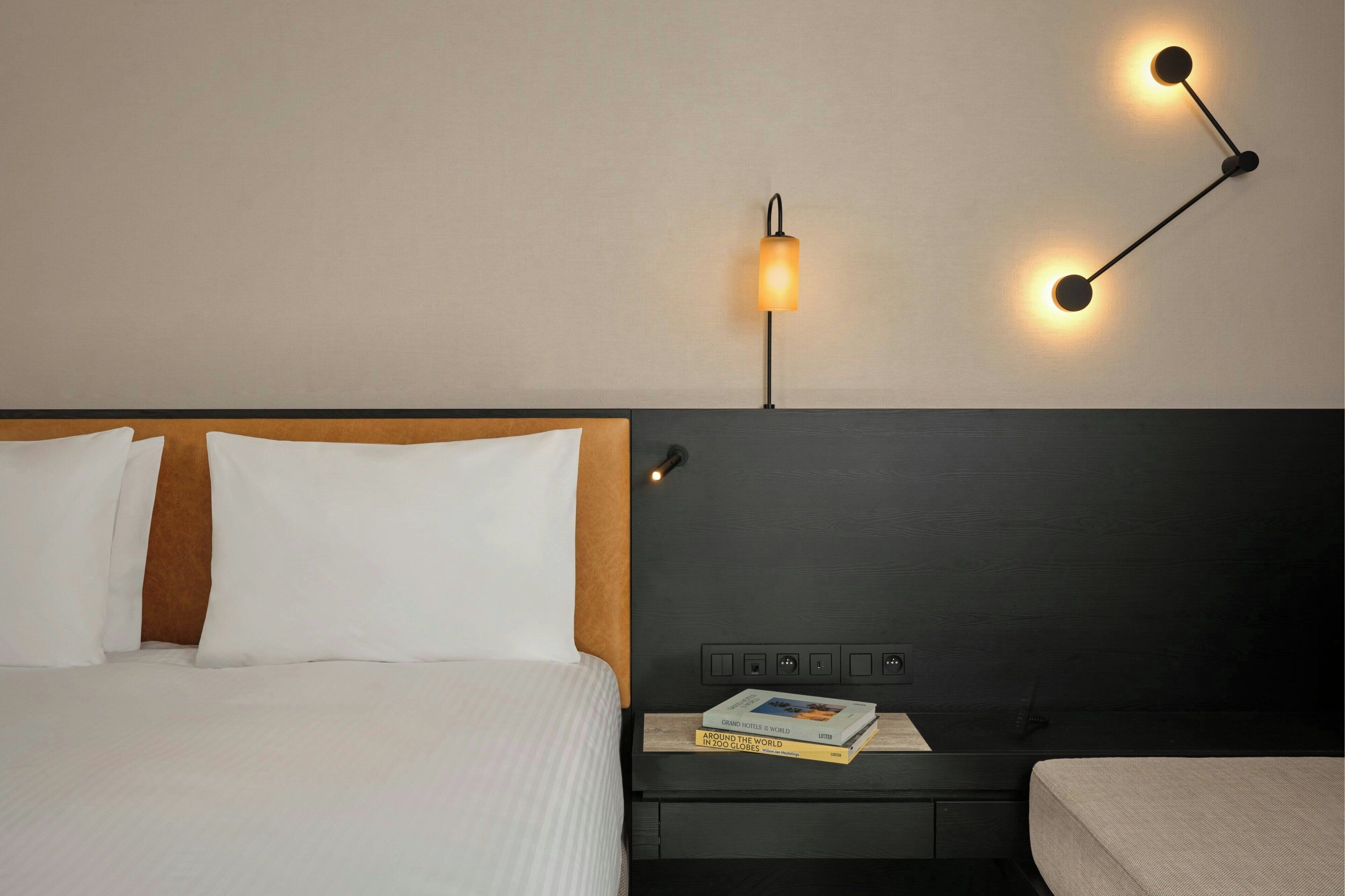 A hotel room with a bed, bedside table, and a wall-mounted lamp.