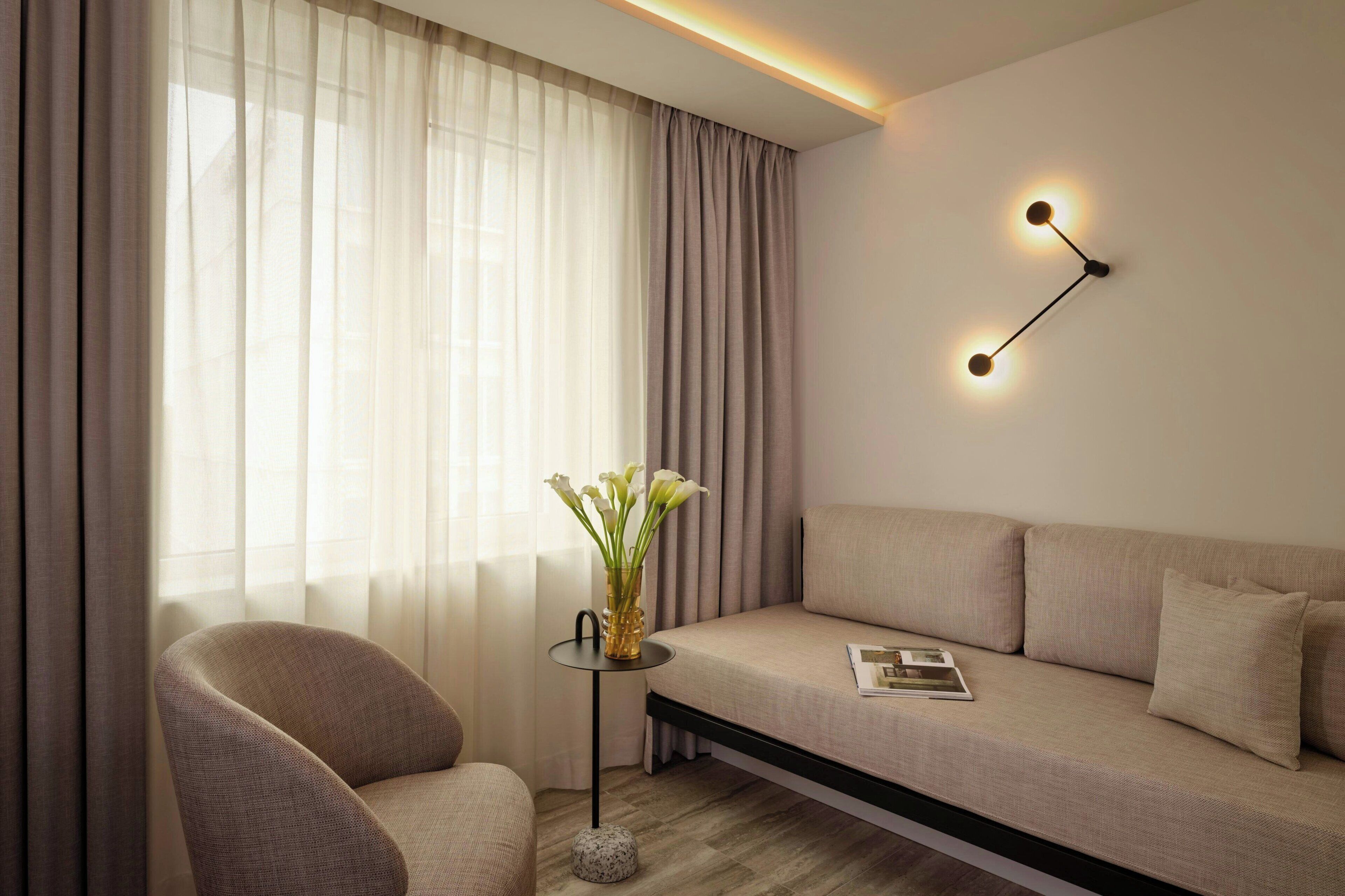 Een moderne woonkamer met een bank, een fauteuil, een klein bijzettafeltje met een vaas en een wandlamp.
