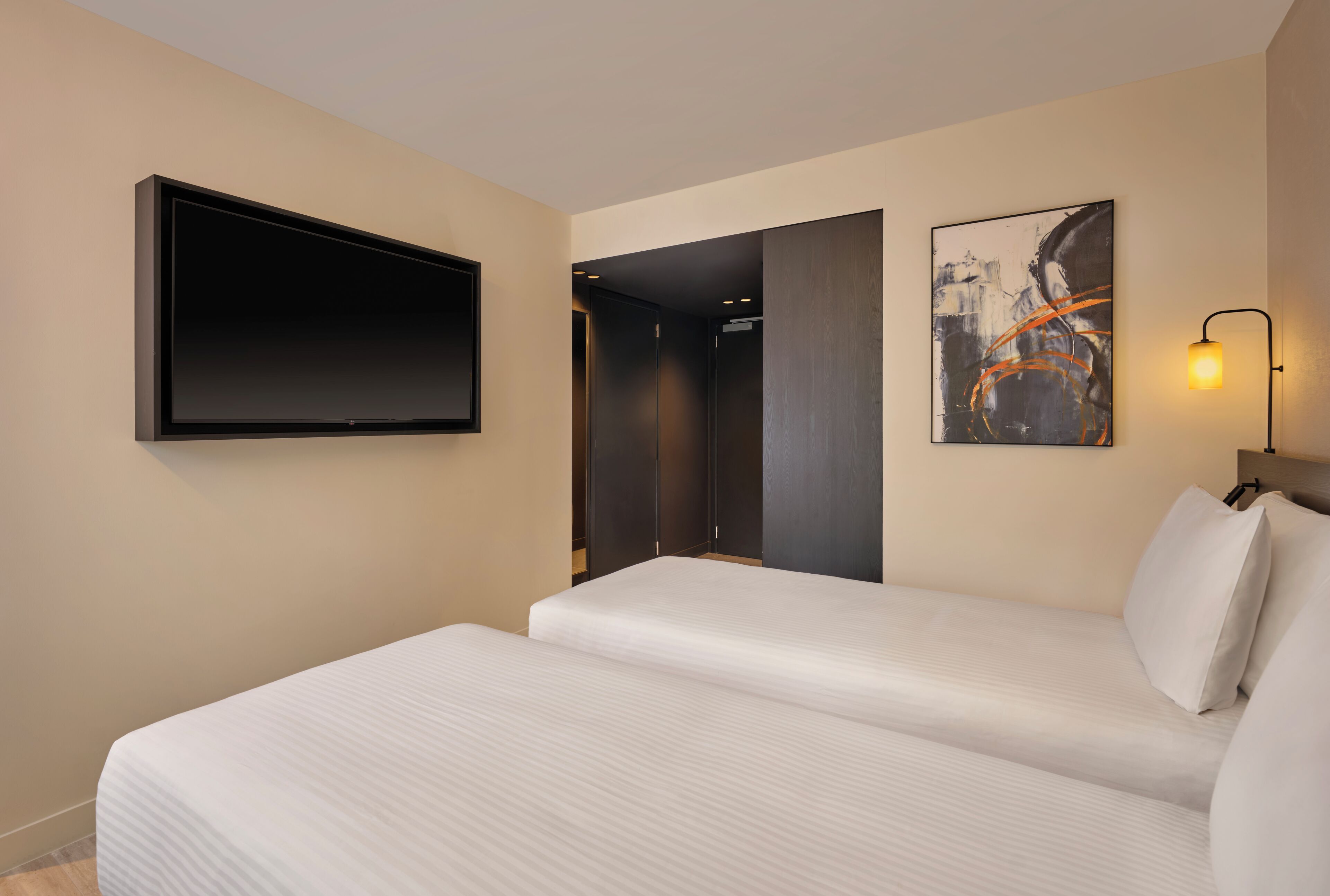 Habitación de hotel con cama, televisión de pantalla plana, un cuadro y una lámpara de pared.