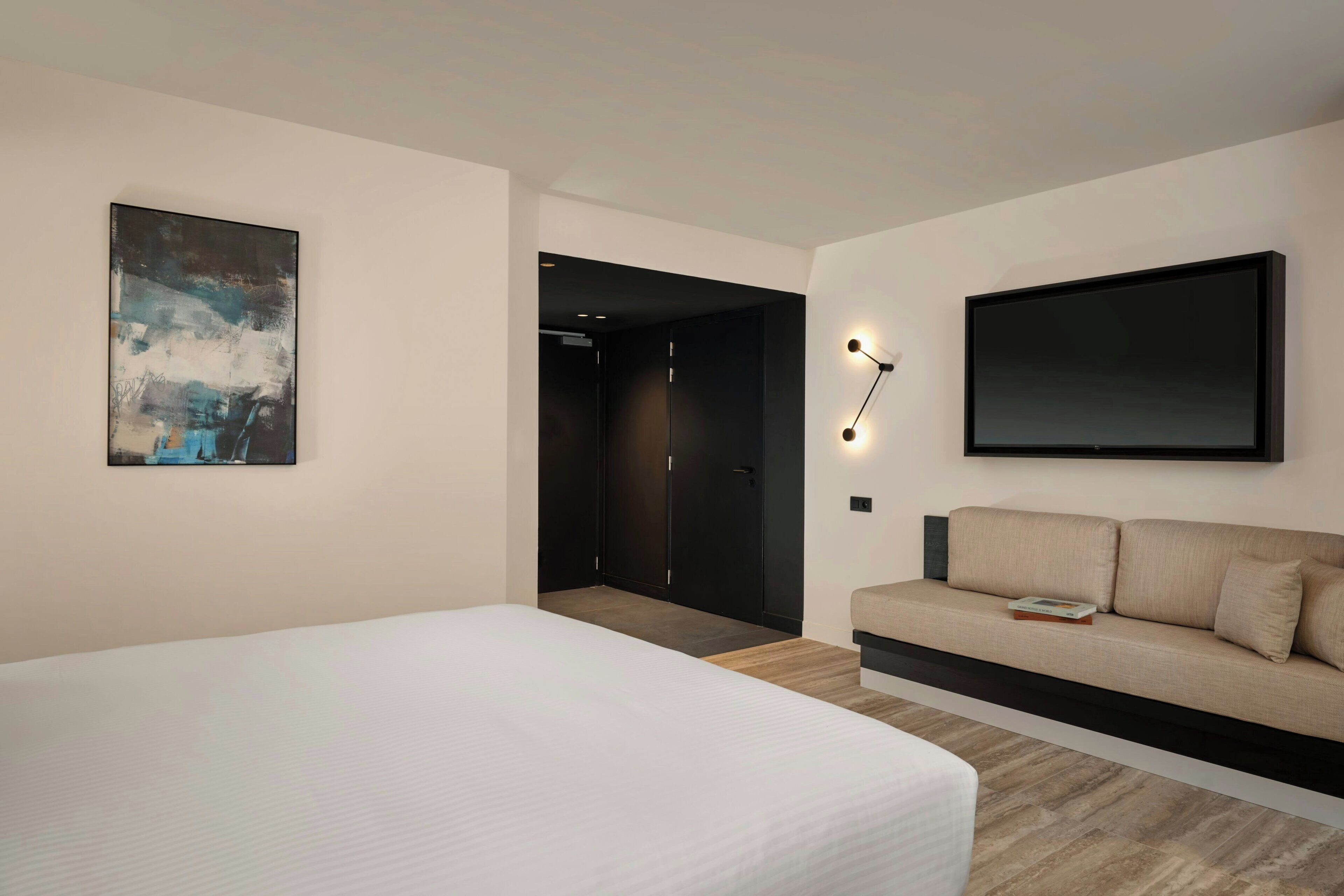 A modern hotel room with a bed, a sofa, a painting, and a TV.