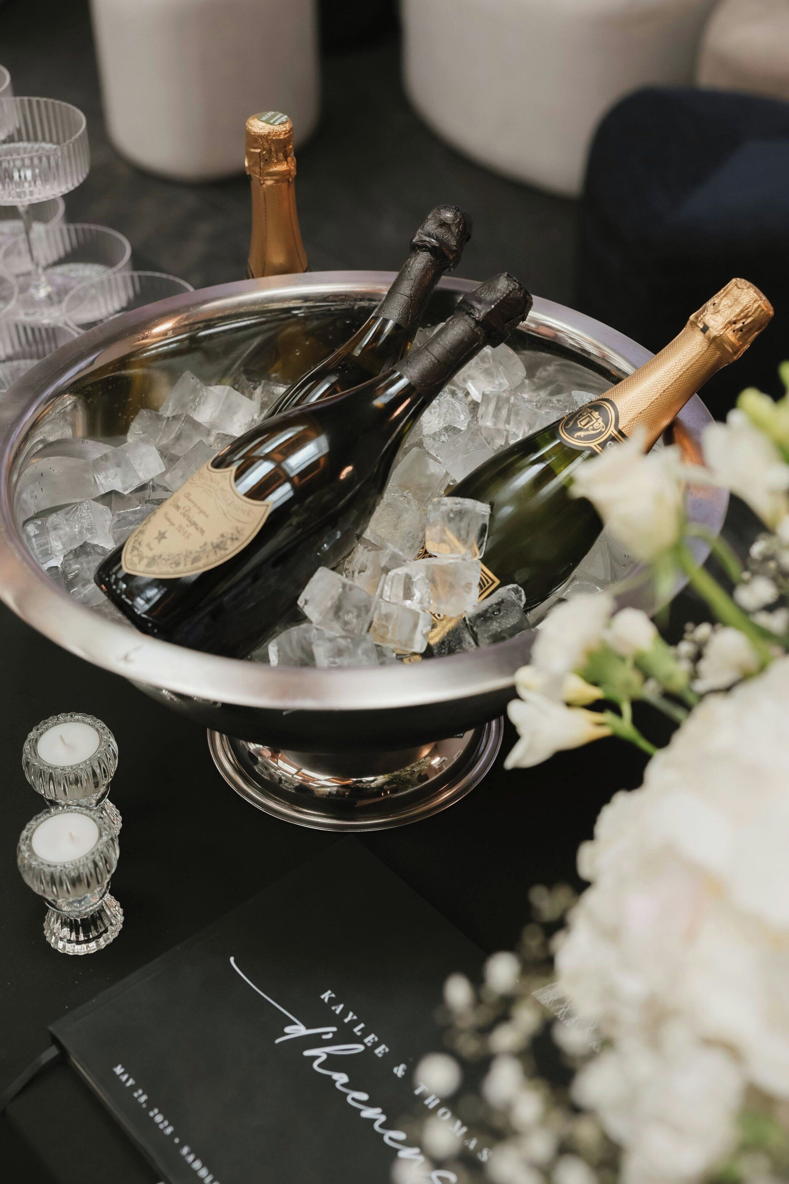 A metal bucket filled with ice and champagne bottles, a candle, and a card with text.