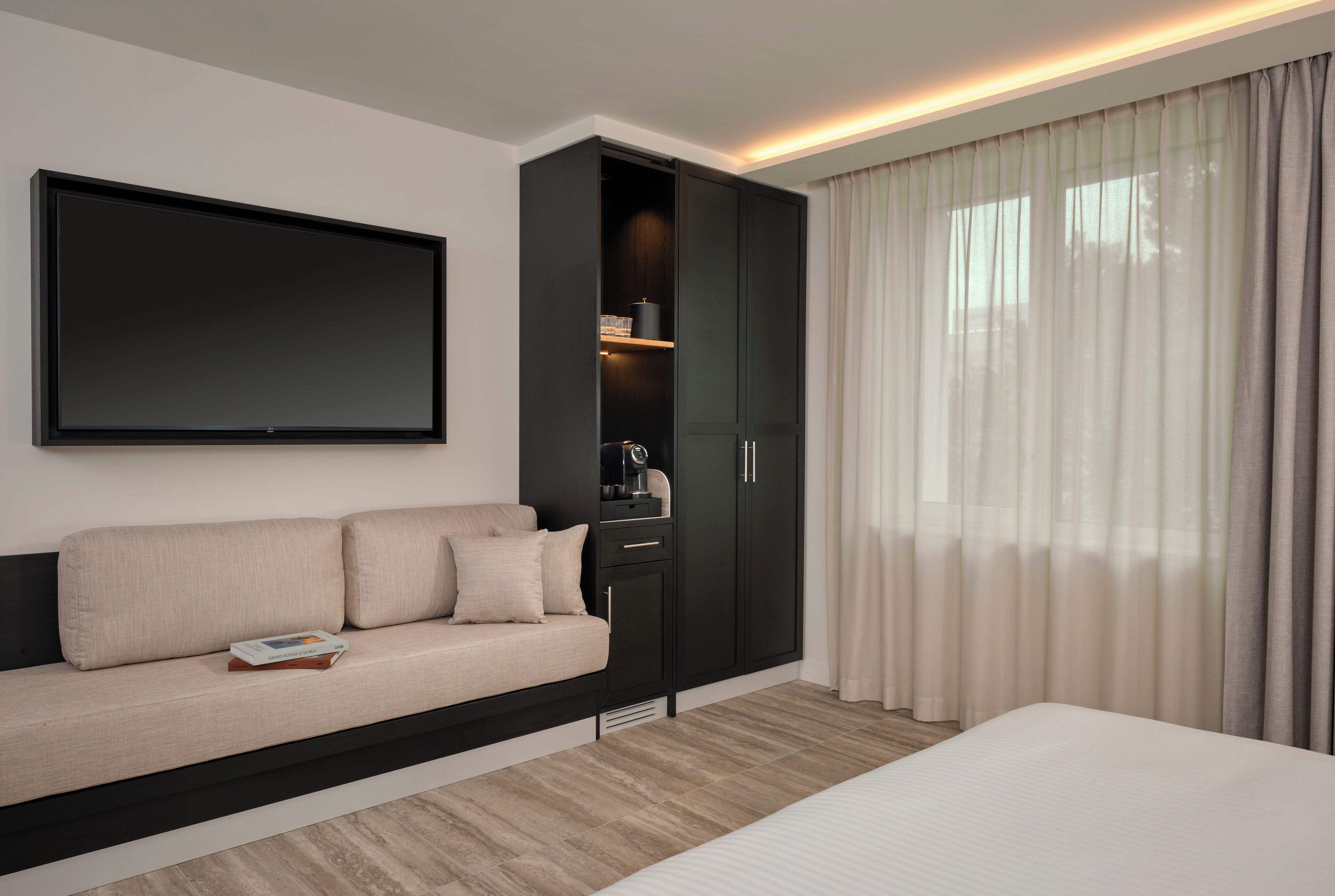 Une chambre d’hôtel moderne dotée d’un grand lit, d’un canapé, d’un téléviseur fixé au mur et d’une armoire avec des étagères intégrées.