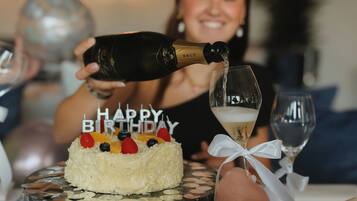 A birthday cake with 'HAPPY BIRTHDAY' candles, a bottle of champagne being poured into a glass, and a person holding a glass.