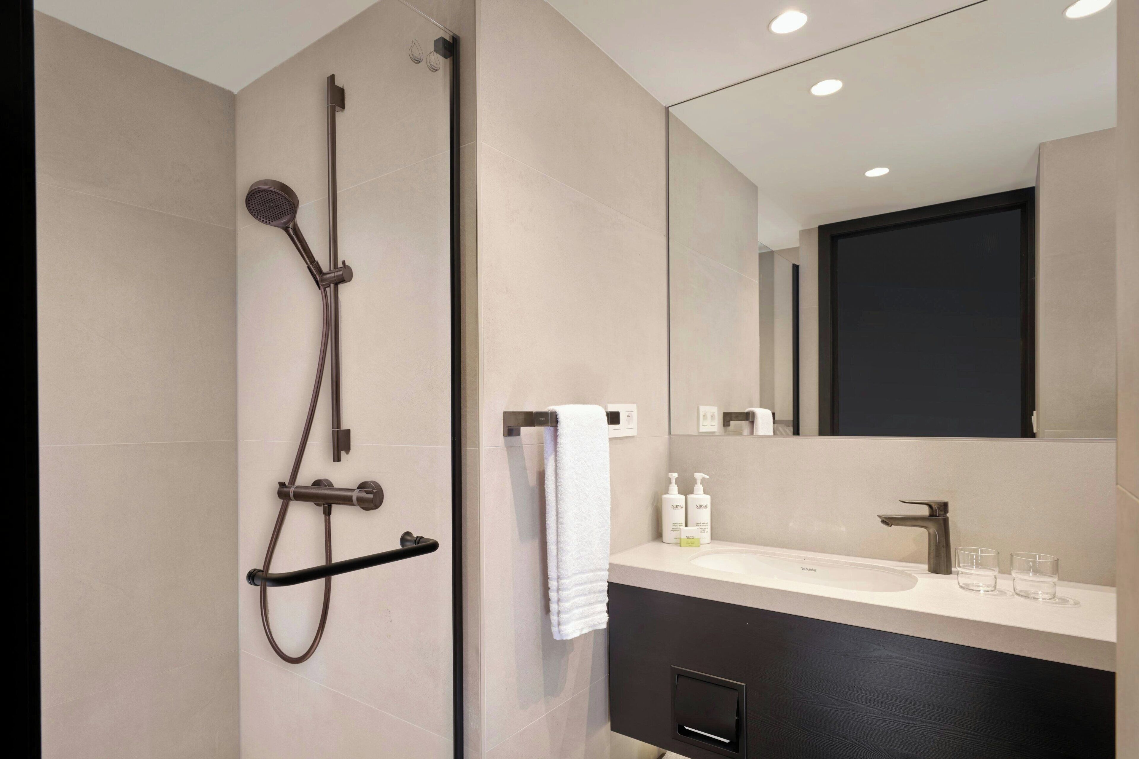 Un baño moderno con ducha, lavamanos y un espejo grande.