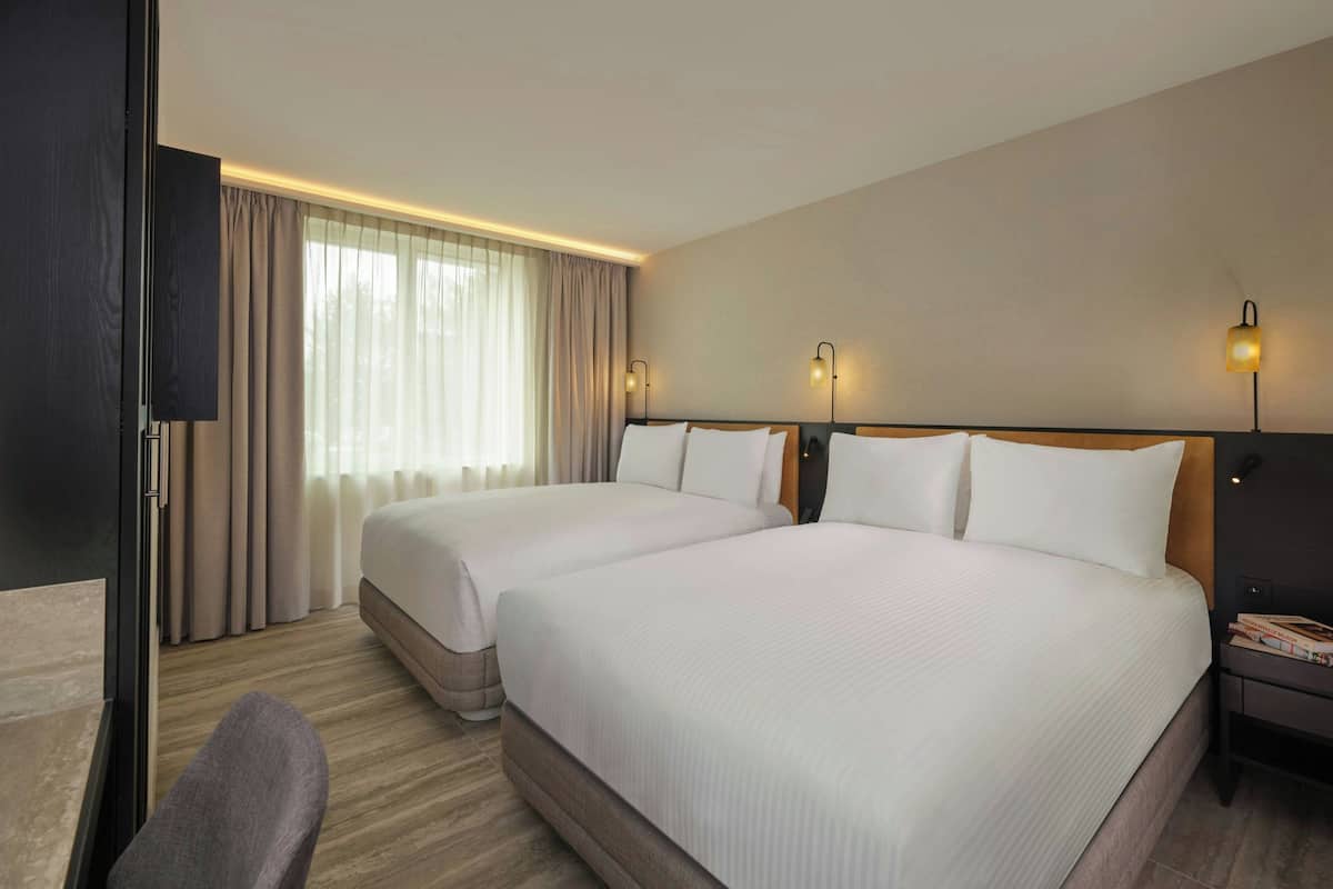 A hotel room with two beds, a TV, a desk, and a chair.
