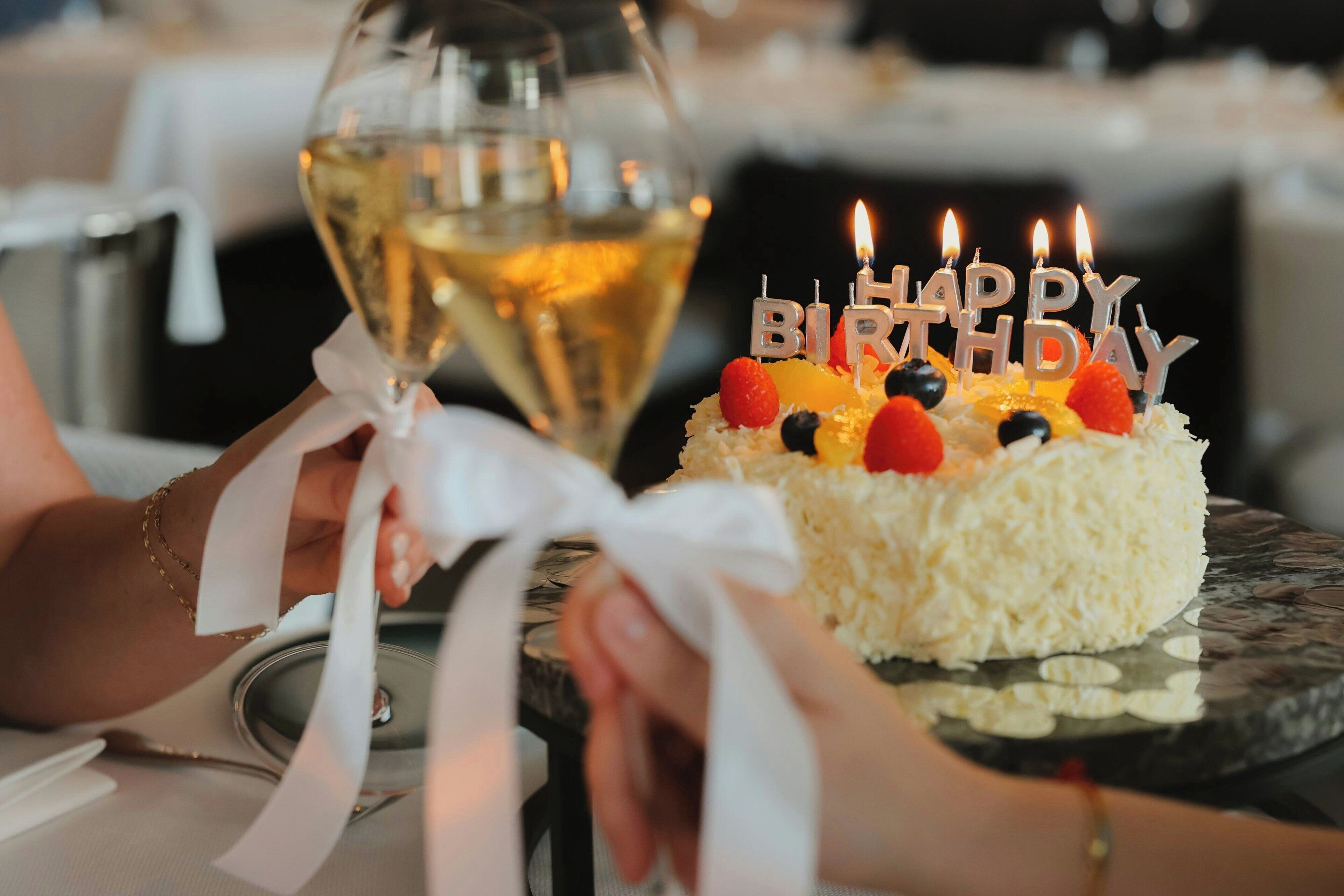 A birthday cake with candles and a glass of white wine.