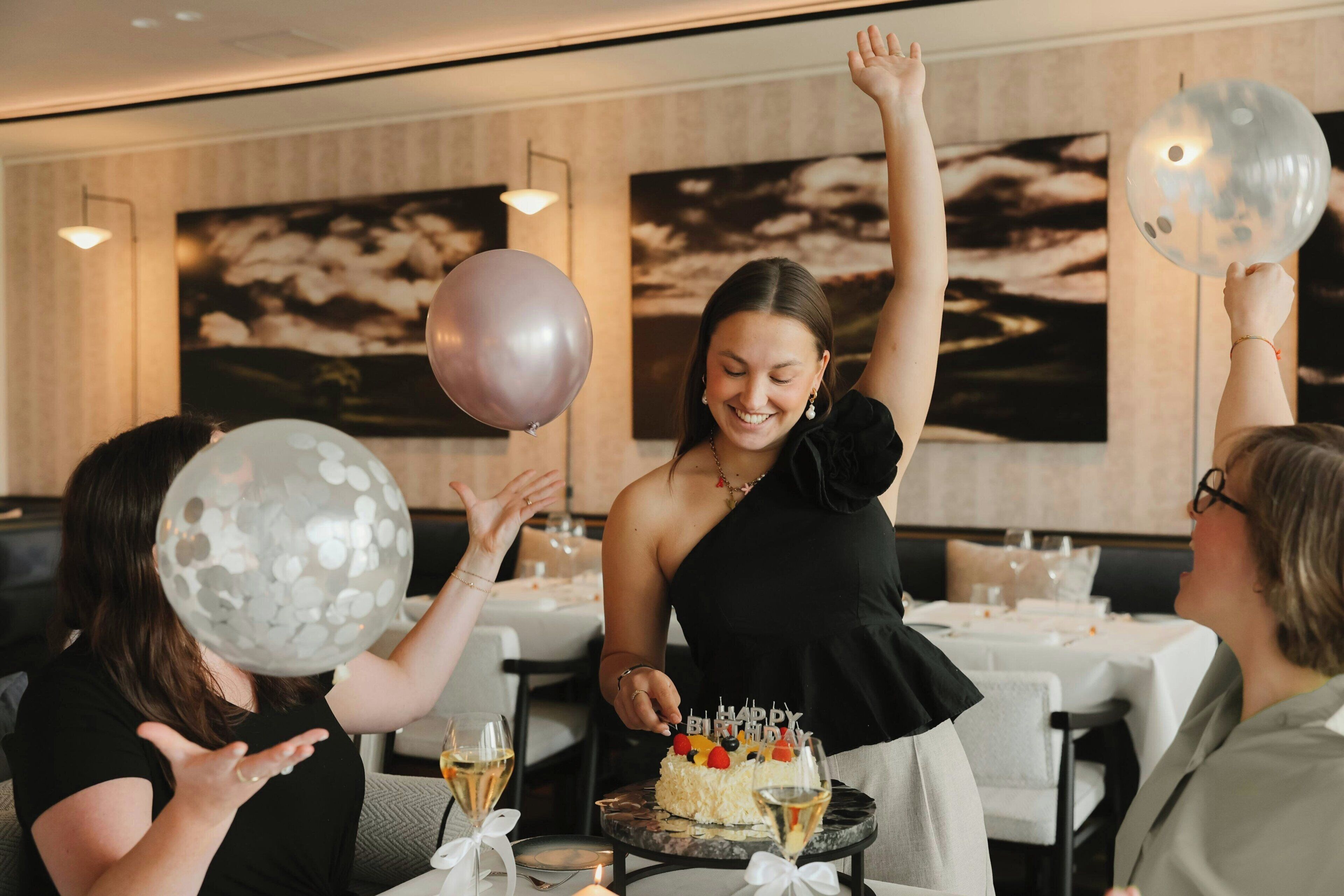 Eine Gruppe von Personen feiert einen Geburtstag mit einer Torte und Luftballons in einem Restaurant.