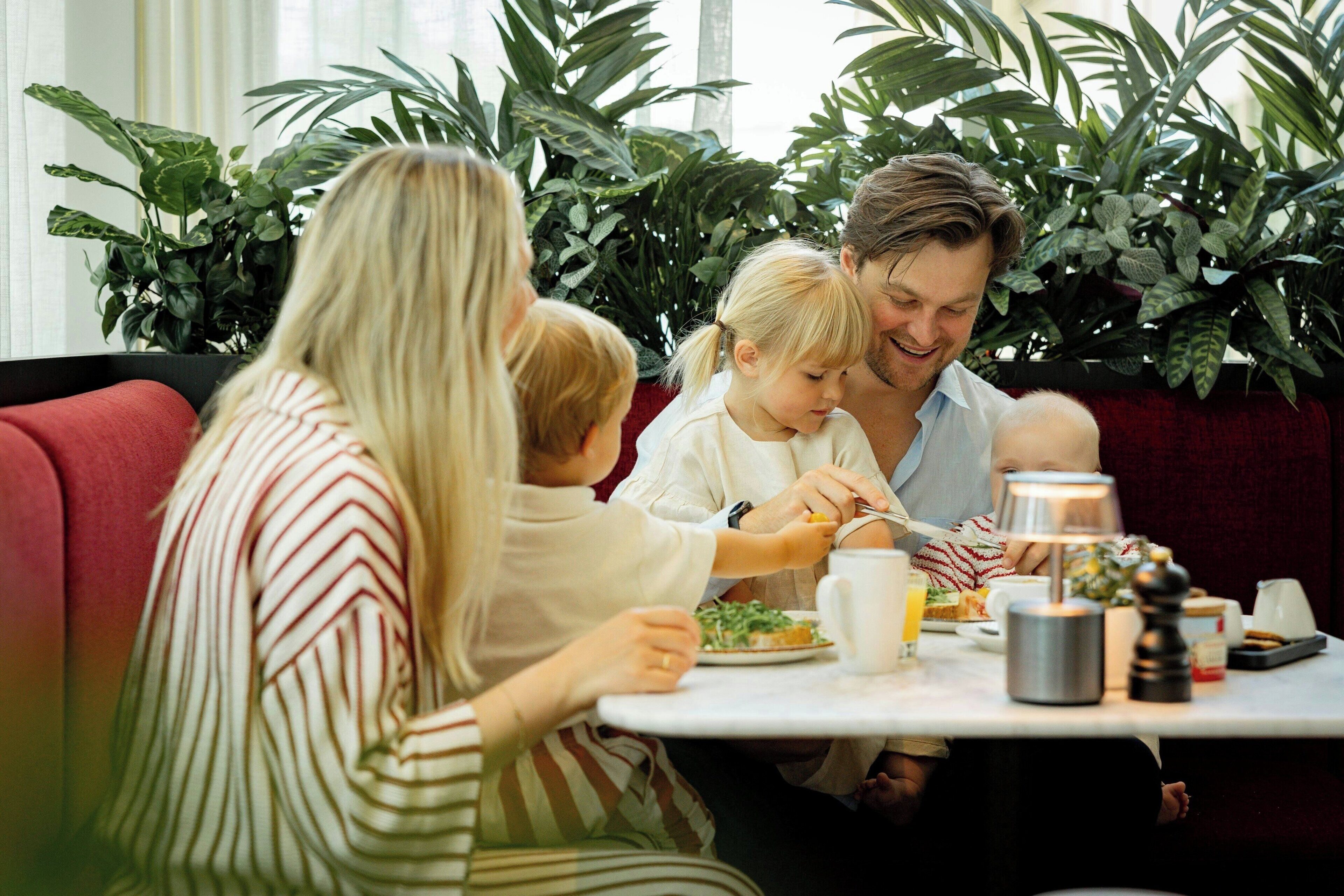 A family dining at a table with a variety of dishes, surrounded by lush green plants.