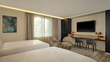 A hotel room with two beds, a desk with chairs, a flat-screen TV, and a painting on the wall.