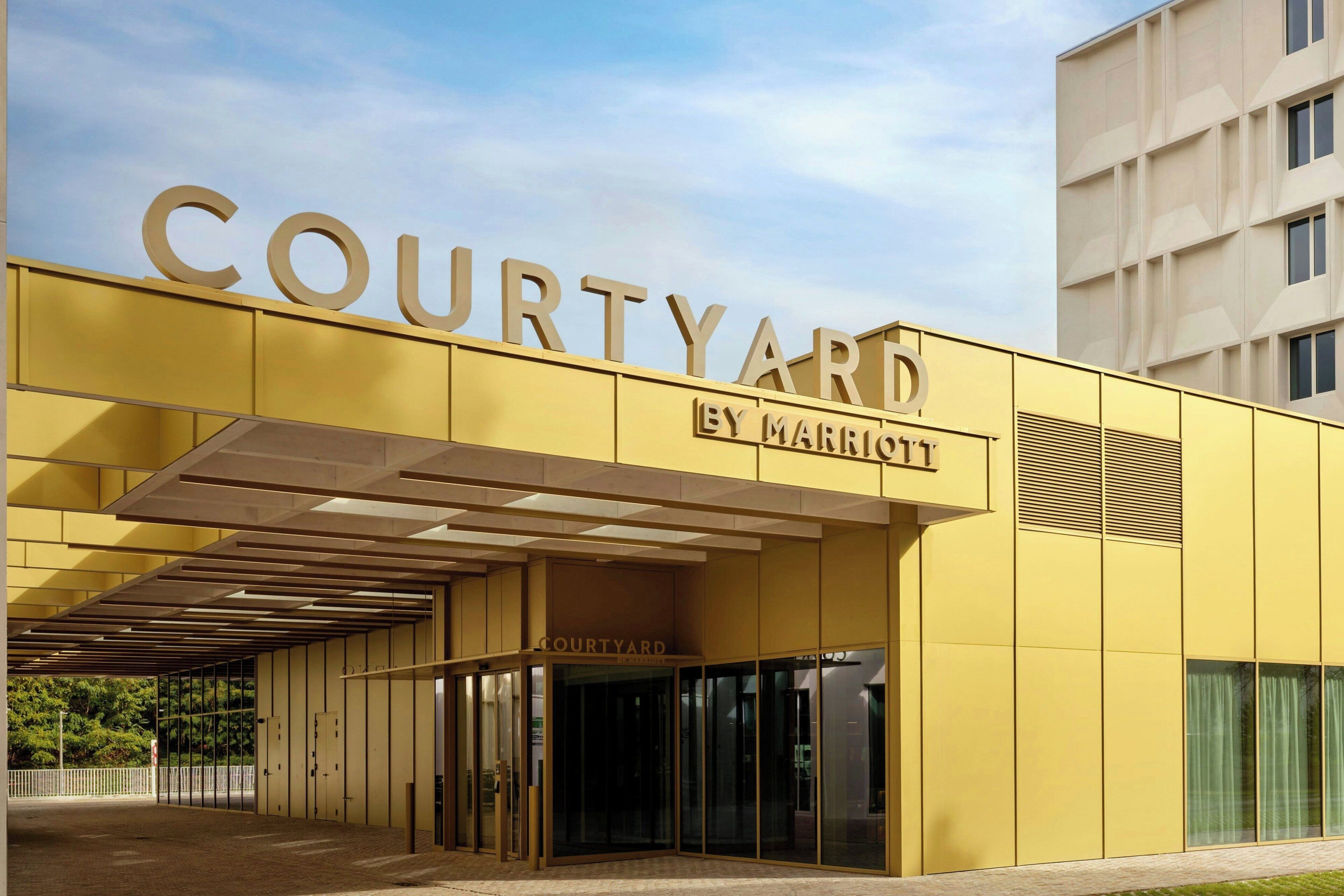 Un edificio moderno con fachada amarilla y el nombre "COURTYARD BY MARRIOTT" visible en grande.